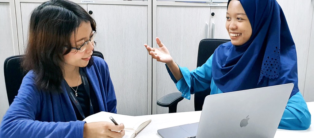 One women interviewing and taking notes and another one answering the questions with a big smile